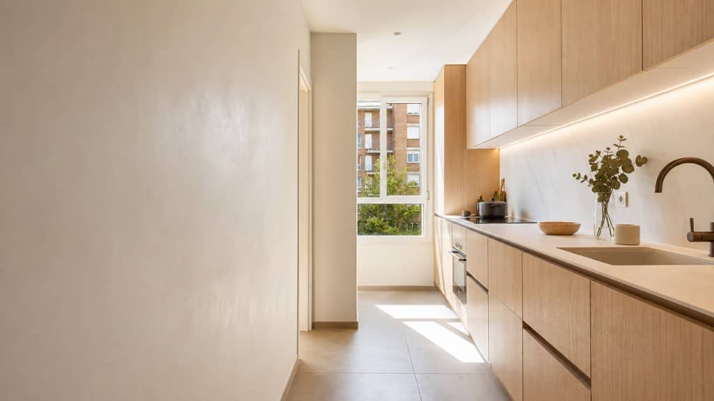 Cocina lineal estrecha de piso reformada con madera clara y encimera de piedra